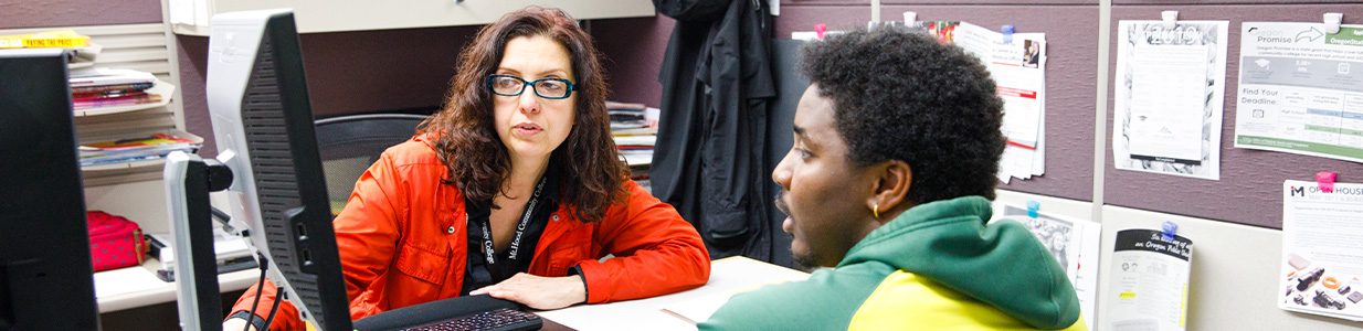 A student talking with an advisor at their desk