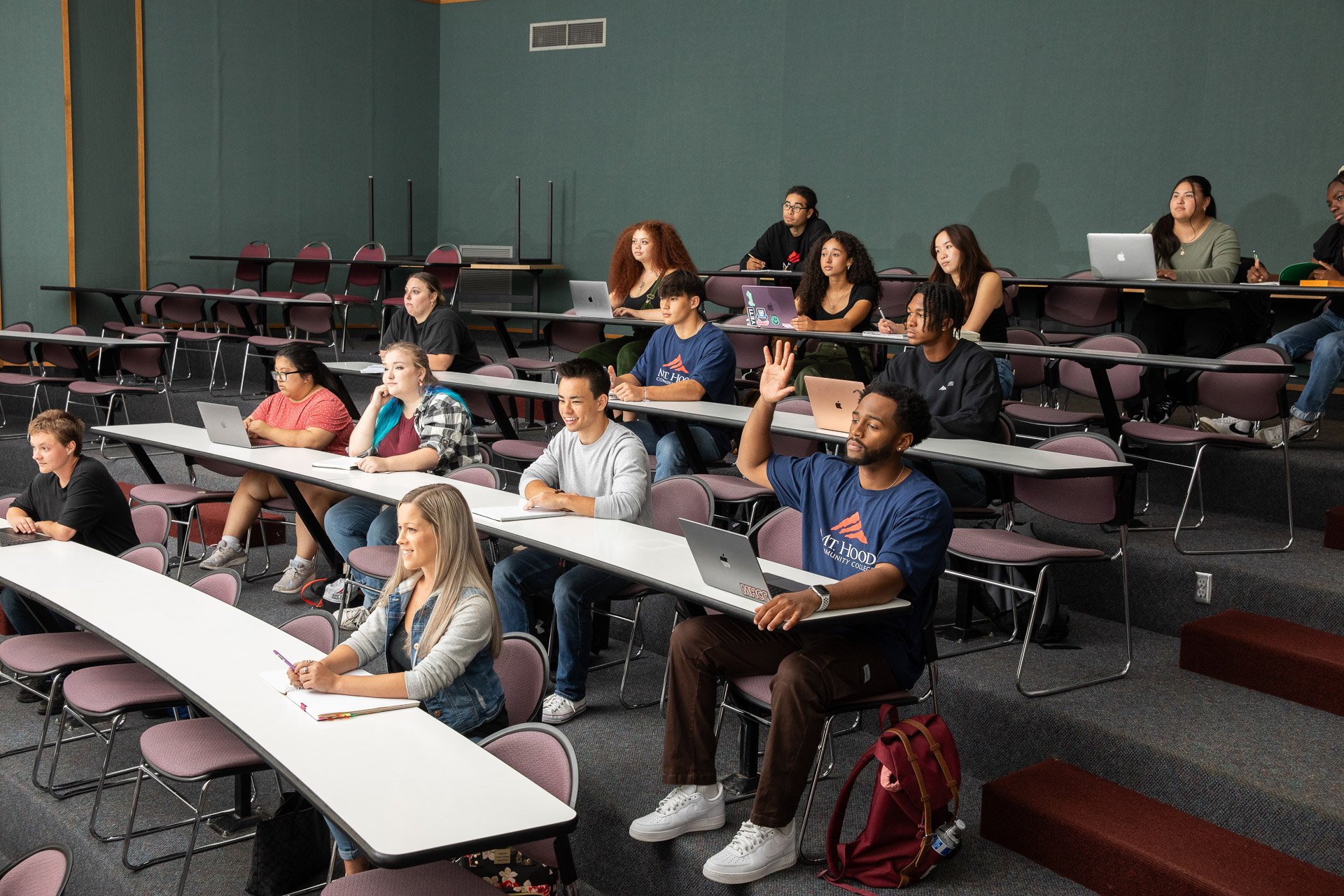Students in a an auditorium-style classroom. One student has their hand raised.